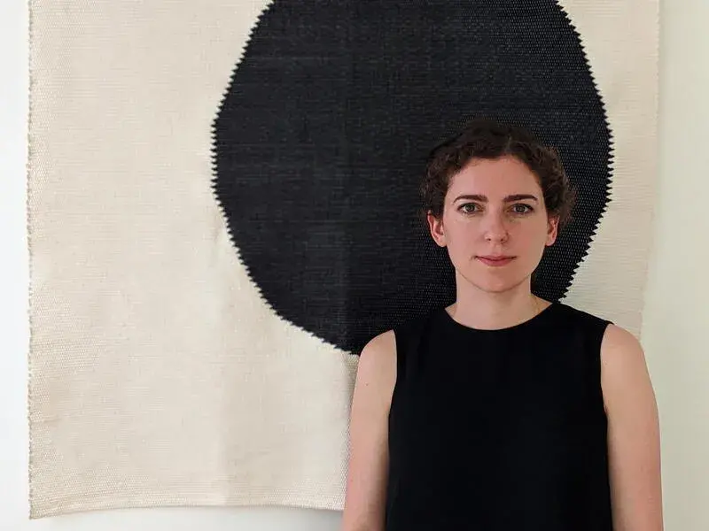 Yasmin Vobis stands in front of a black and ivory tapestry 