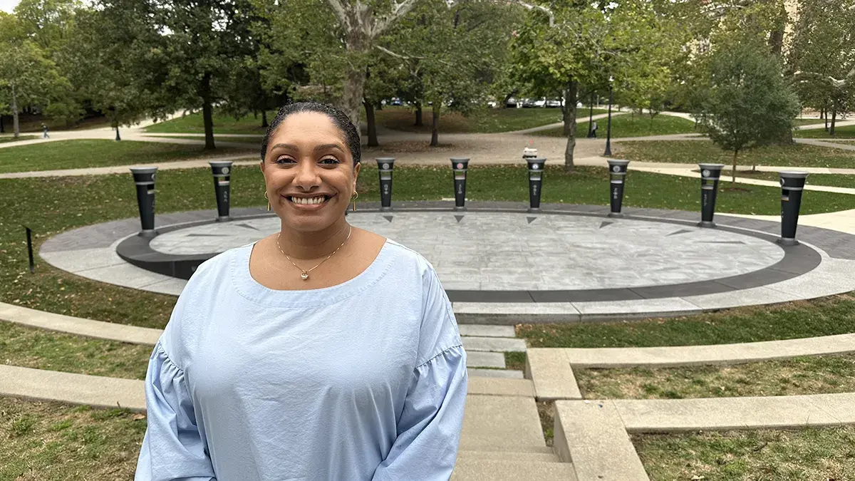 A photo of Parisa Ahmadi, a woman with medium colored skin and dark hair pulled back standing in front of a plaza lined by black monuments
