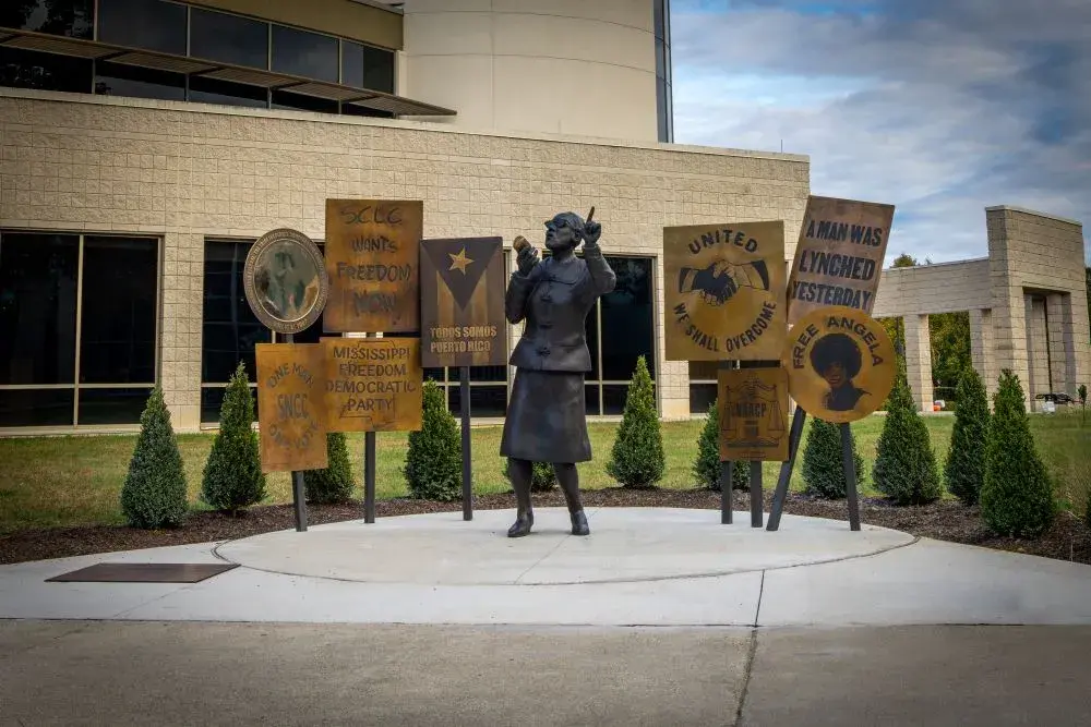 Outdoor bronze sculpture of a woman speaking with posters behind her