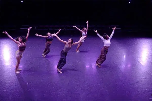 Five people on a theater stage dancing.