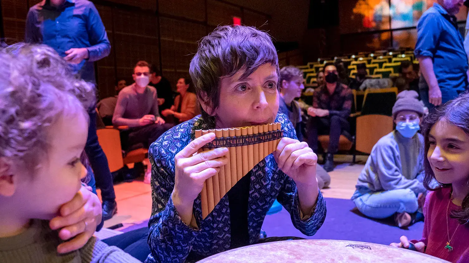 A woman blows into an instrument as young children watch