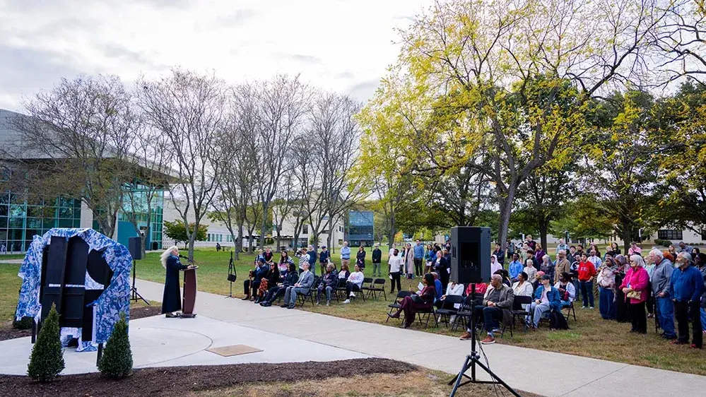A crowd of people listens to artist Dana King speaking in front of her cloaked statue of Ella Baker