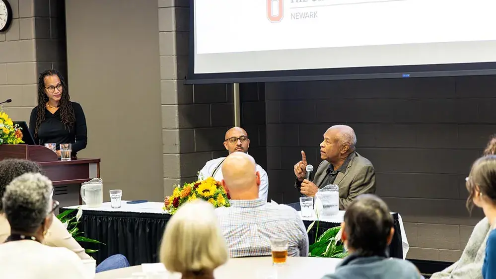 Several people speak to an audience sitting at tables
