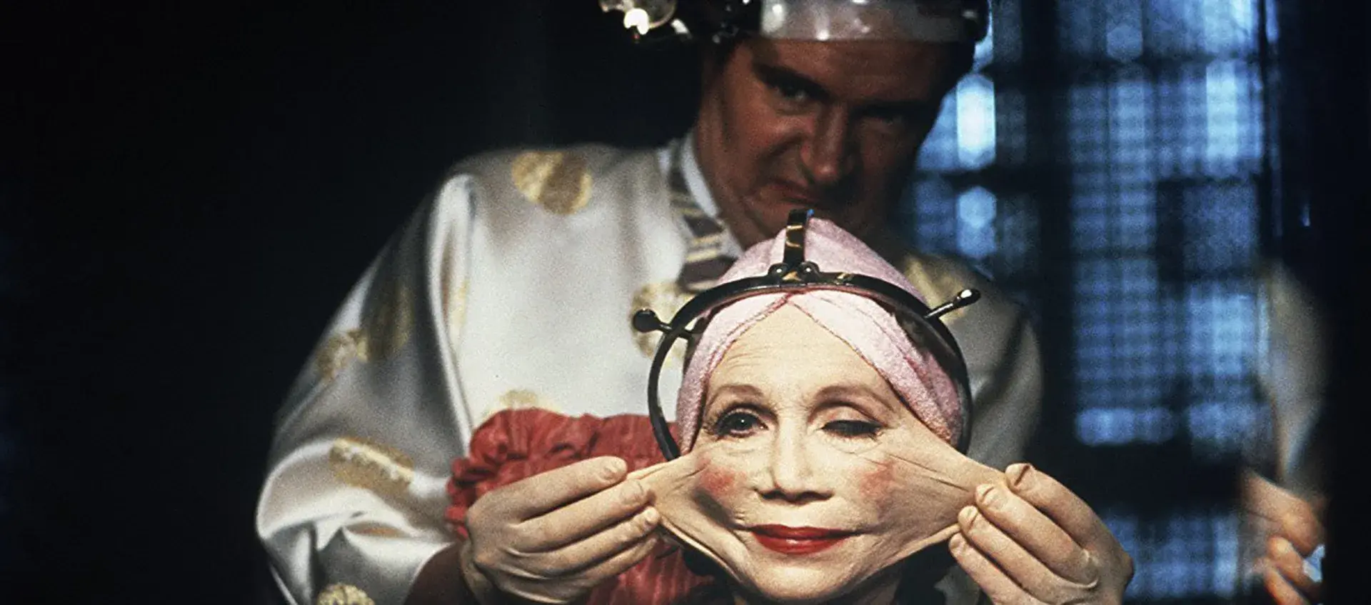 Still from Brazil of a person extensively stretching the cheeks of a woman 