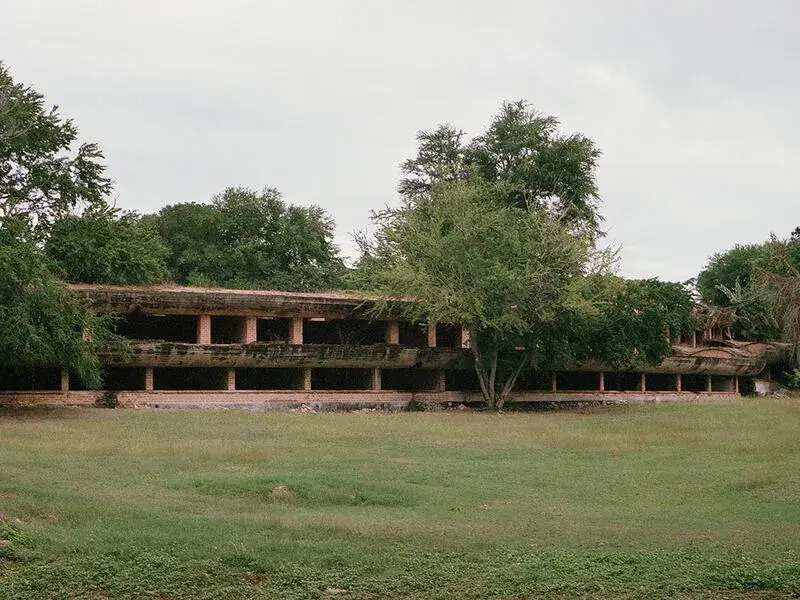 A low slung open structure on a green field with surrounding trees