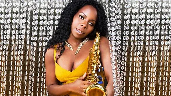 Image of Tia Fuller, a Black woman wearing a yellow dress, holding a saxophone