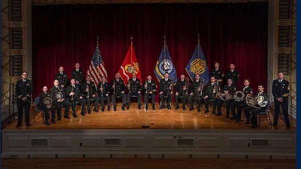 A semicircle of people in uniform holding instruments with flags behind them