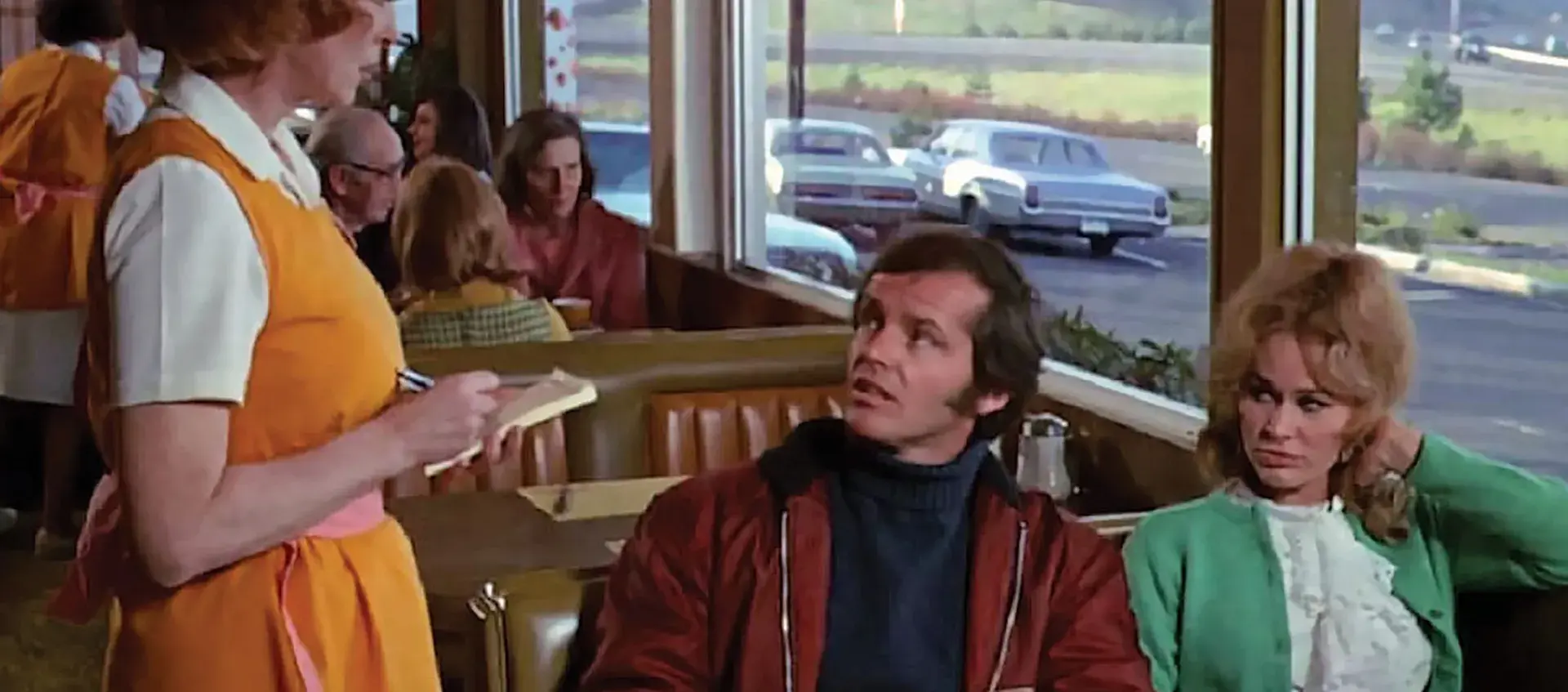 Film still of a man and a woman sitting in a restaurant booth while a waitress takes their order