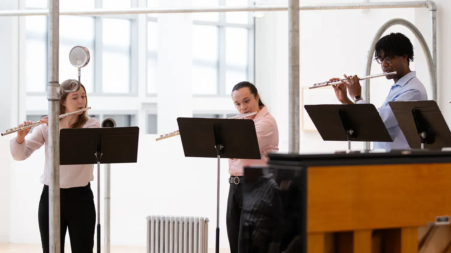 Four students with music stands play flutes amid silver pipes from an art installation by Nancy Holt. A piano is in the foreground.