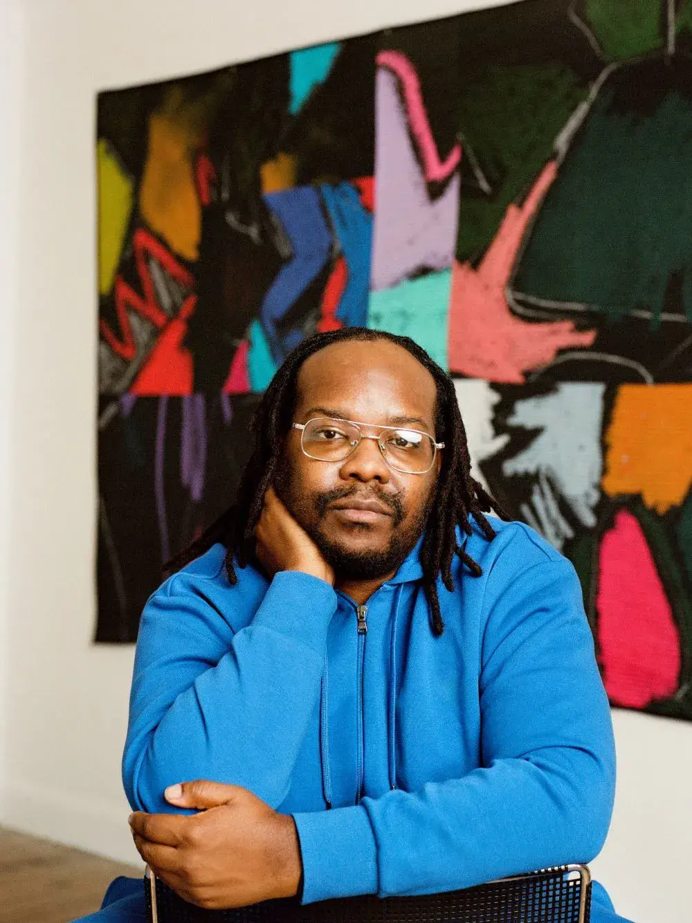 Headshot of Julian Jamaal Jones, a Black man wearing glasses, in front of an abstract artwork