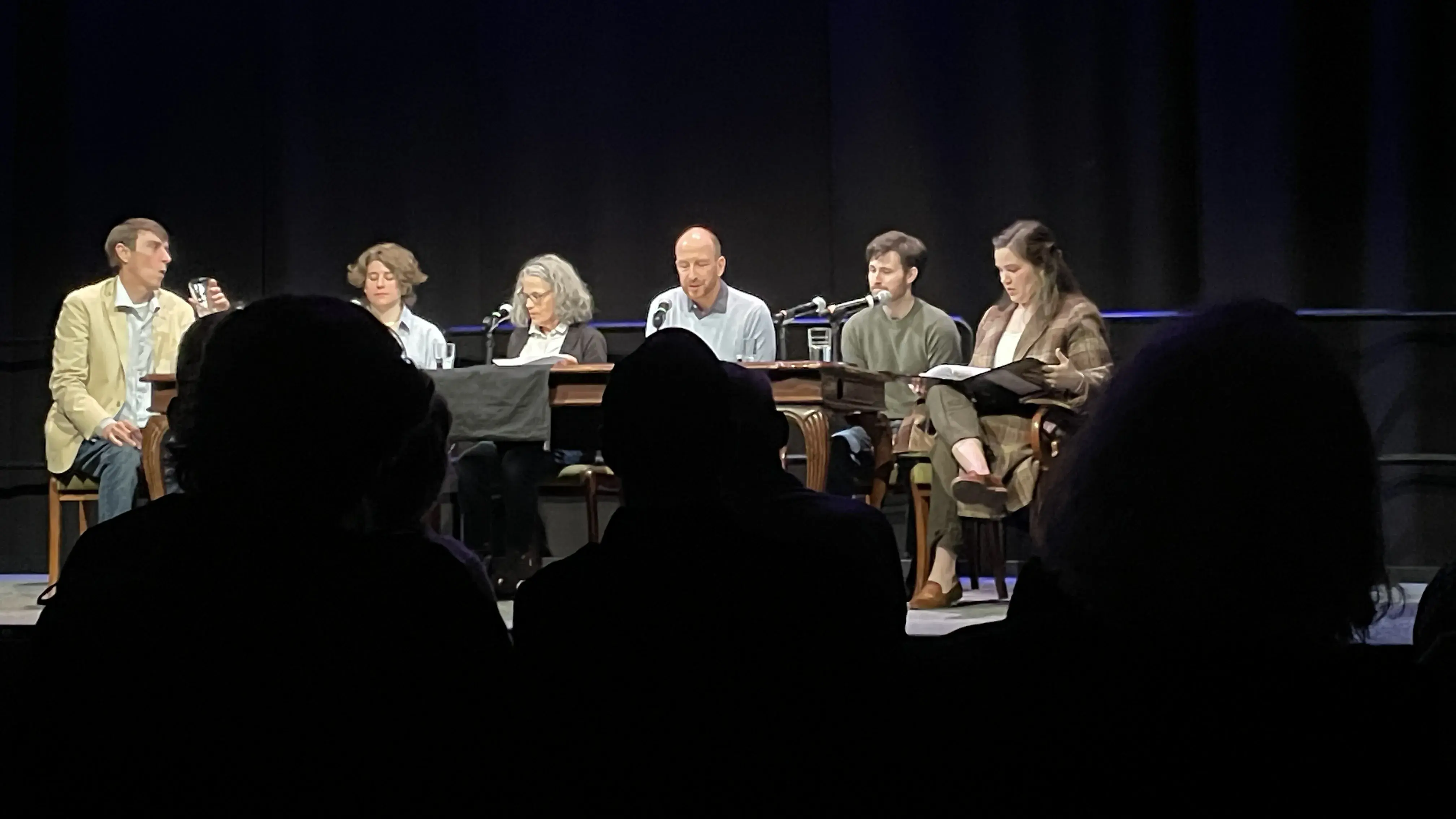 Small group of people sitting on stage at a table in a darkened space