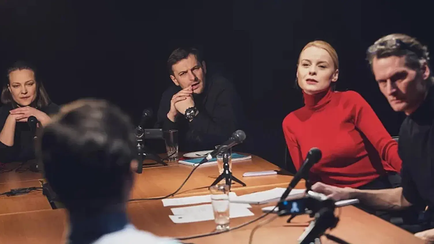 Several people sit around a table with microphones and papers in front of them