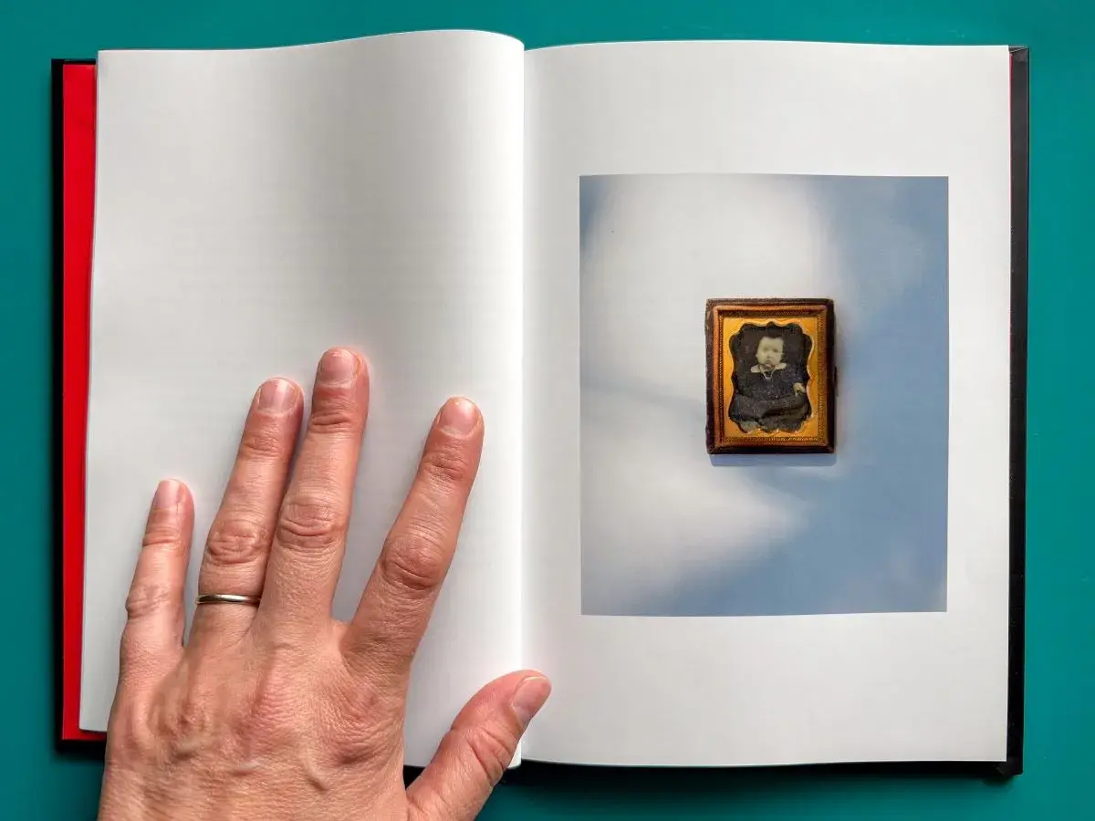 A hand holds open a book with an image of a vintage framed photo on the right side