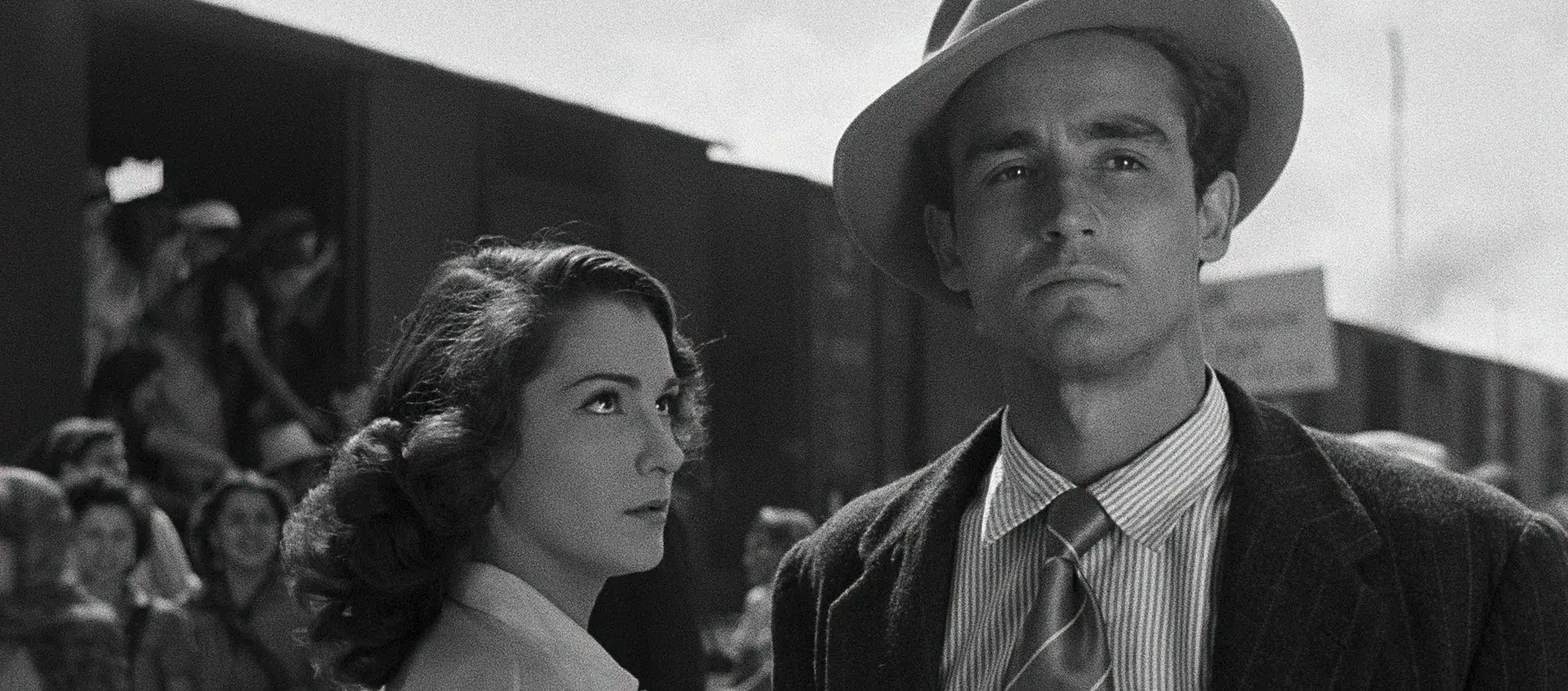 A woman stands looking at a man, behind them many people are leaving a train boxcar.