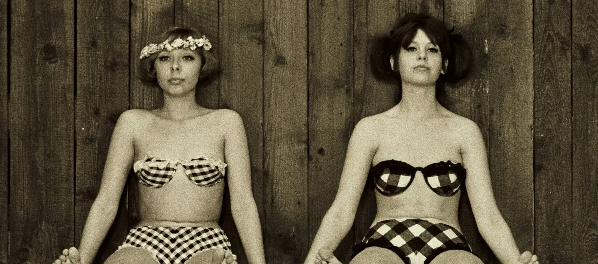 Two women in retro bikinis sit on the ground next to eachother.