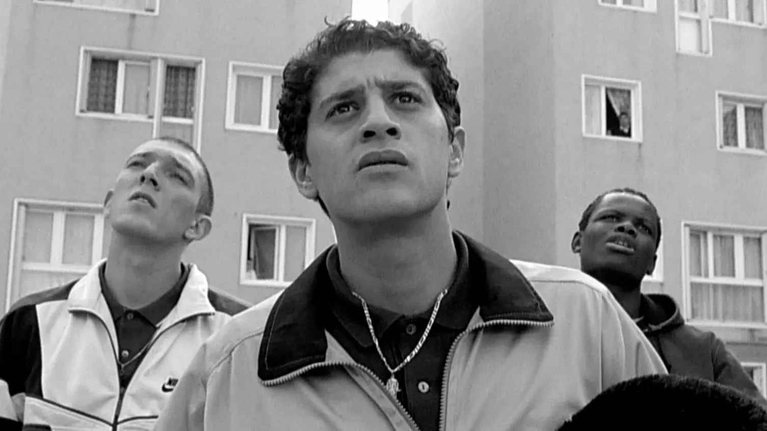 Three men stand in front of a housing project.