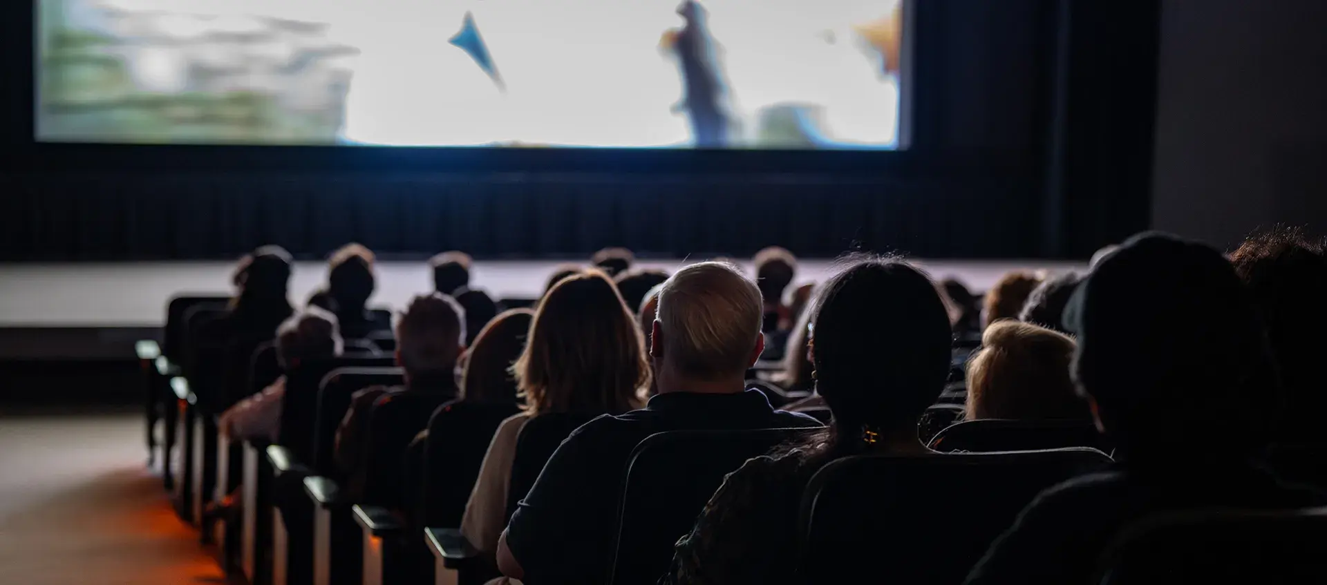 A movie theater audience looks ahead at a film screen.