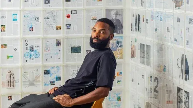 Tavares Strachan sits in front of his artwork on a wall