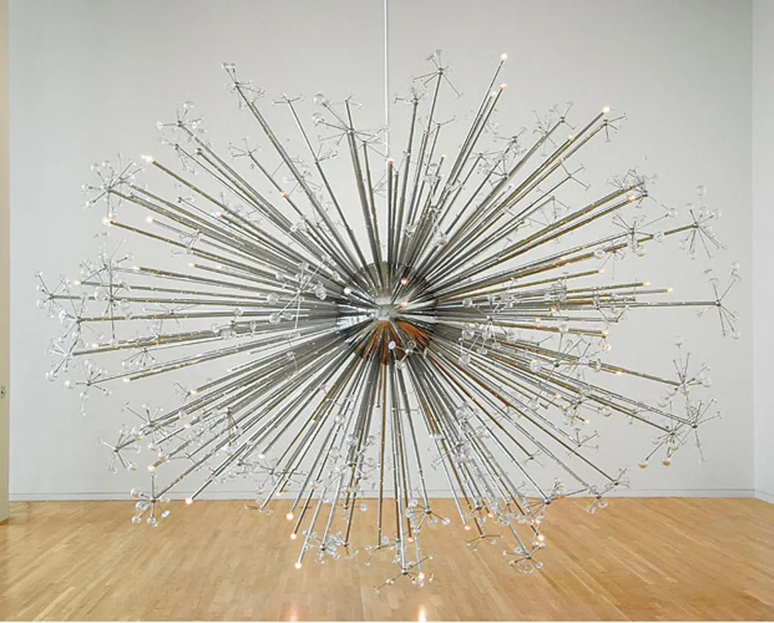 A large metal and glass sculpture is suspended just above a wooden floor.