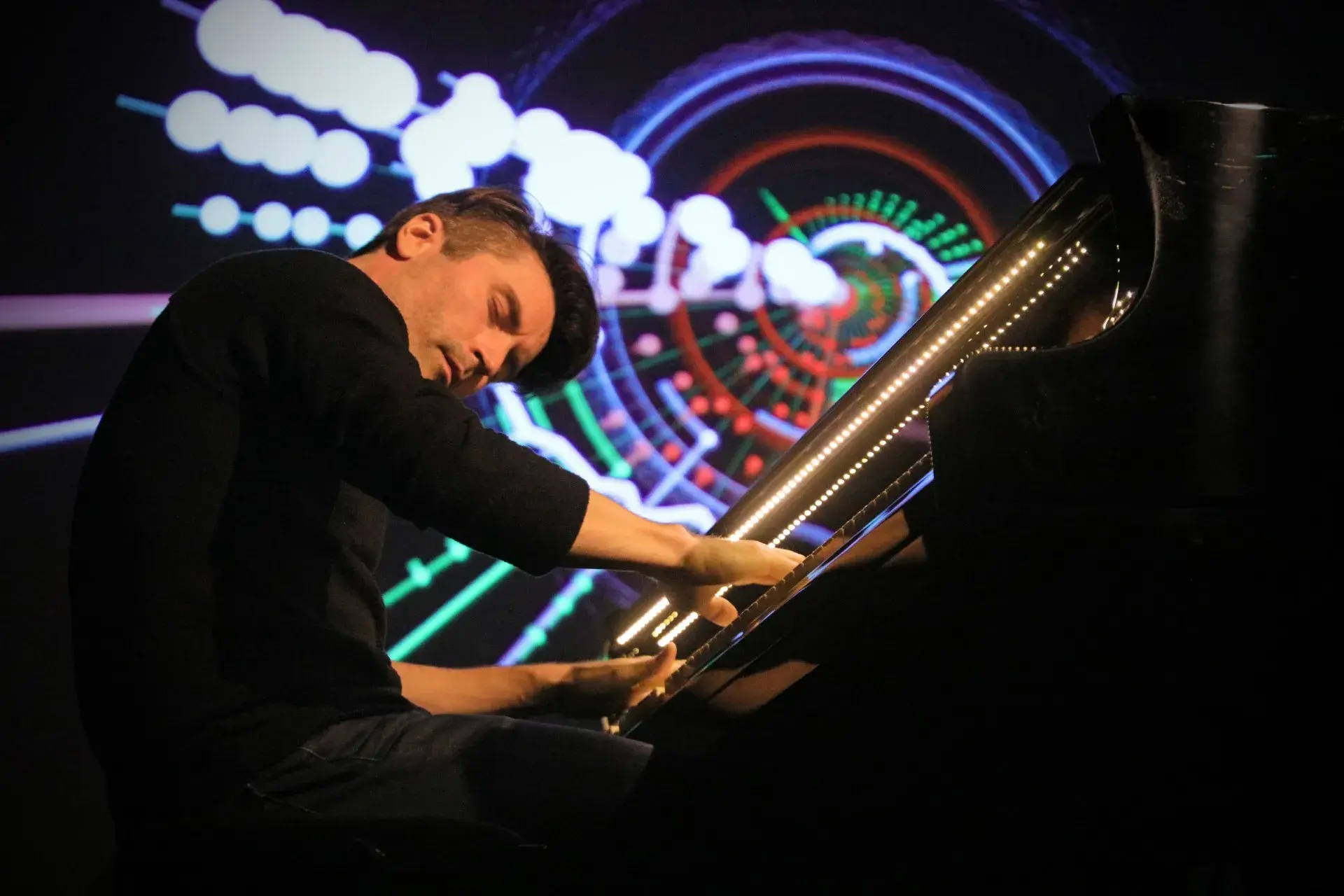 Dan Tepfer plays the piano in front of a dark, abstract backdrop 