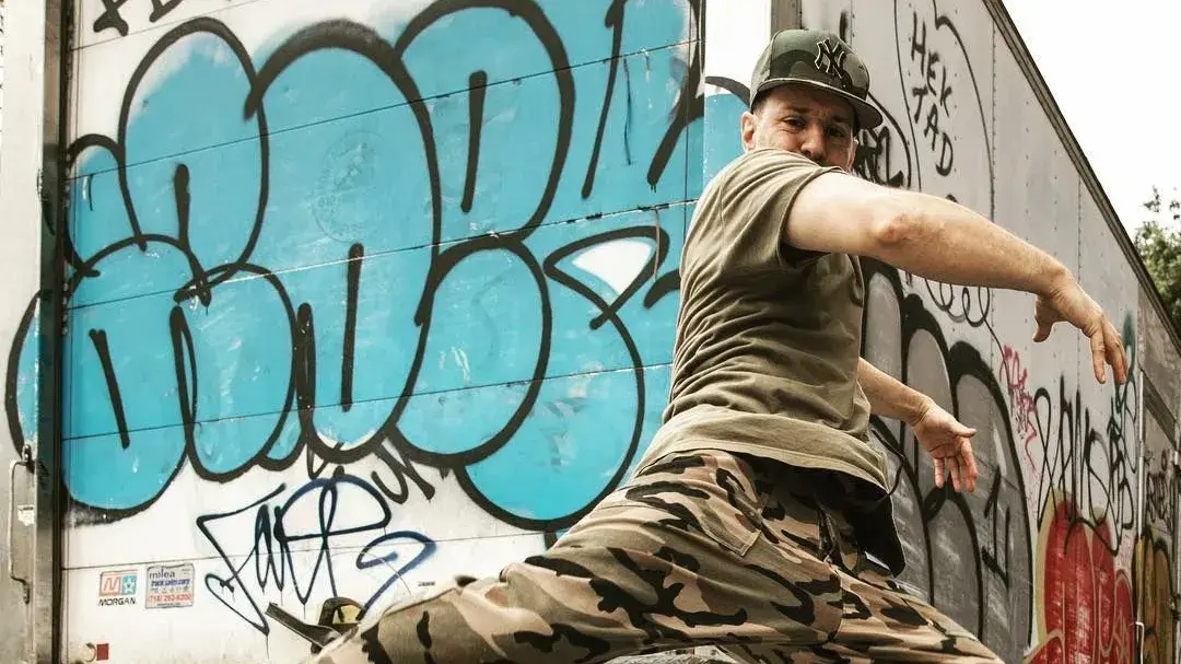 A man is leaping in the air in front of a box truck covered in grafitti.
