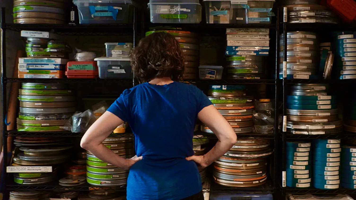 A woman stands facing shelves full of film reel canisters.