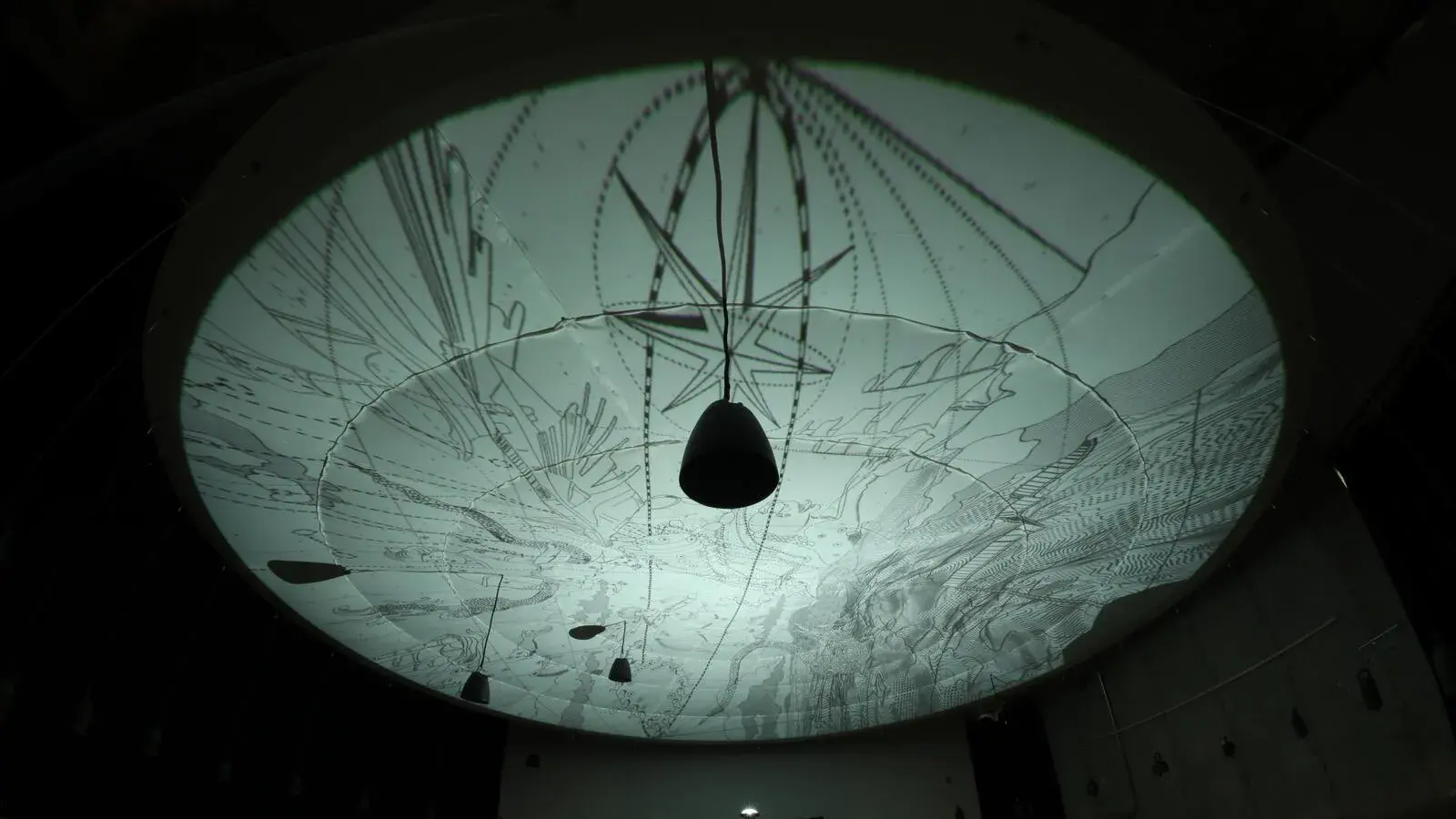 Pale aqua circular shape with drawings on it projected on a ceiling with speakers suspended down