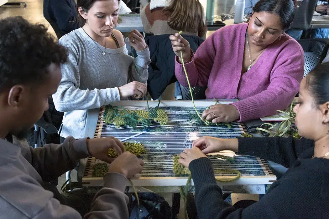 Students weave yarn through a small tabletop loom