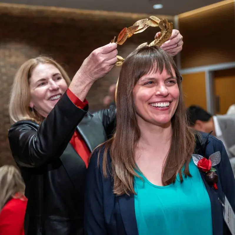 Kate Shannon, a white woman with long straight dark hair, stands while golden laurels are placed on her head
