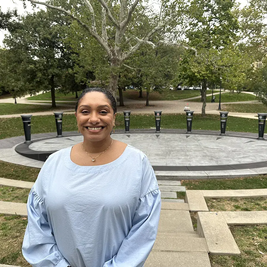 A photo of Parisa Ahmadi, a woman with medium colored skin and dark hair pulled back standing in front of a plaza lined by black monuments