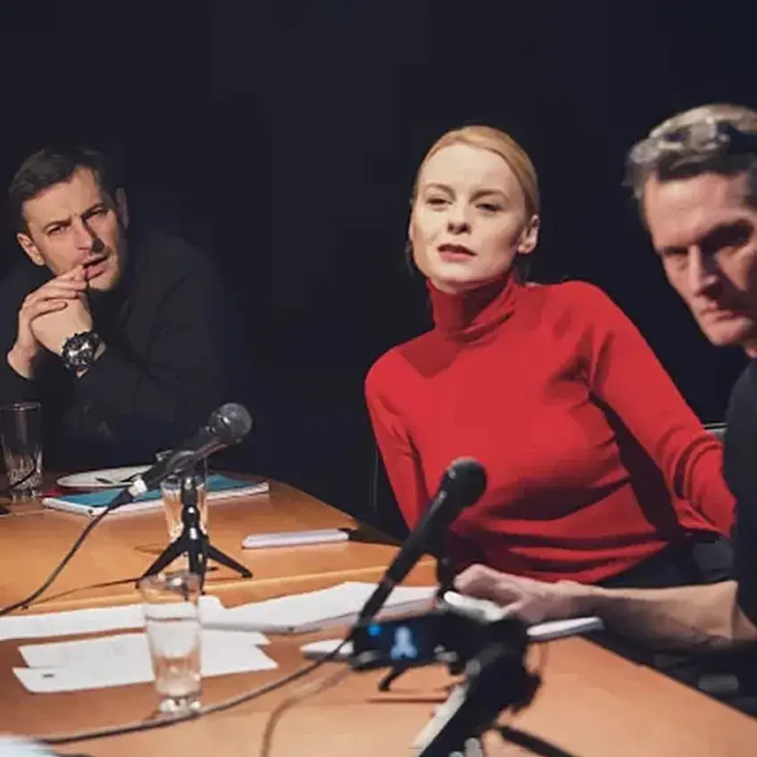 Several people sit around a table with microphones and papers in front of them