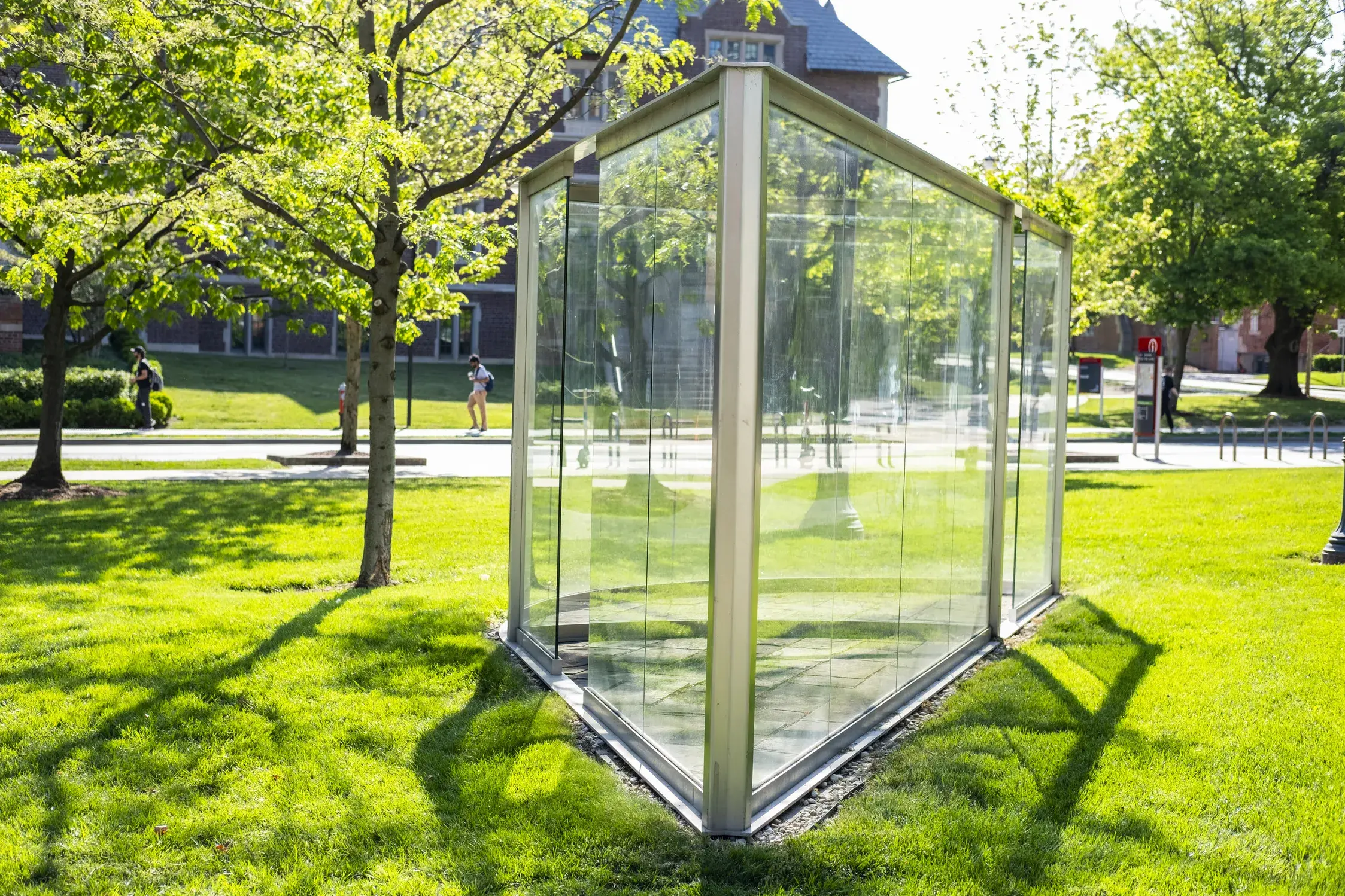 Large glass panes within a metal frame come to a point in the foreground and extend back. The sculpture sits in a grassy area.