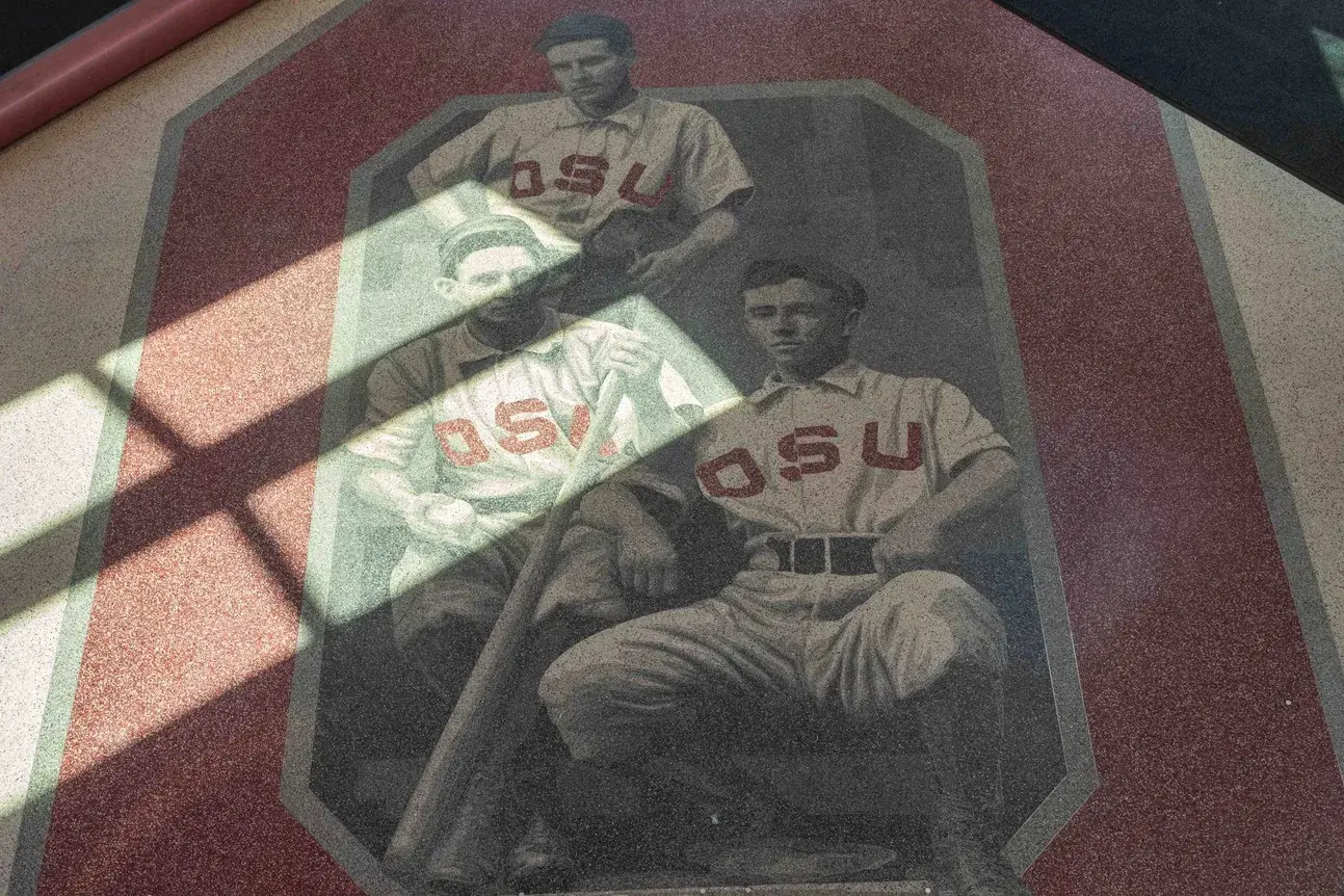 Floor design in grayscale and red shows 3 historical baseball players wearing OSU uniforms positioned within a red block O. There is light from windows on the floor.