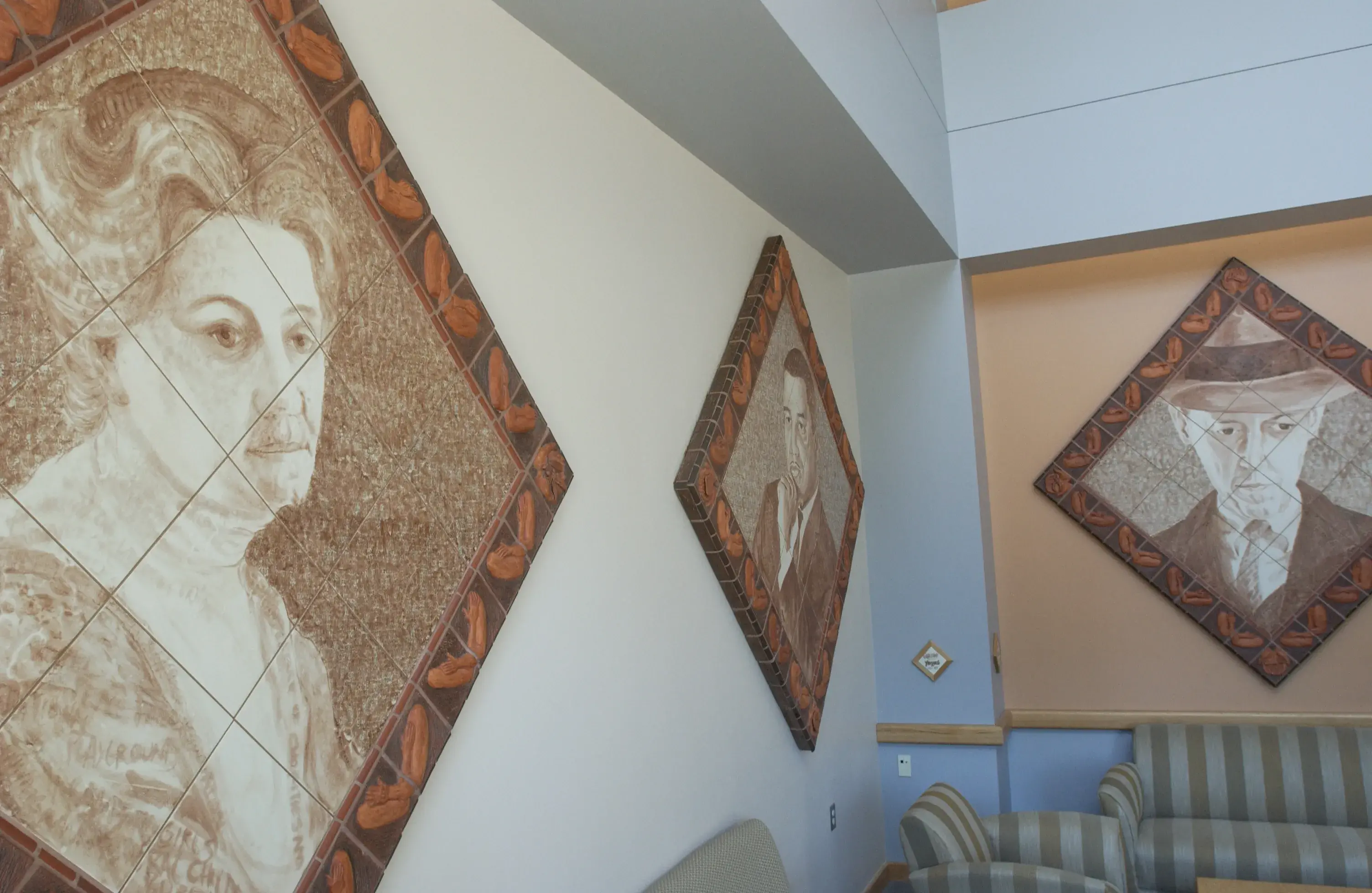 3 diamond-shaped artworks on 2 walls depict a historical person's face on each of them. There is one woman and two men.