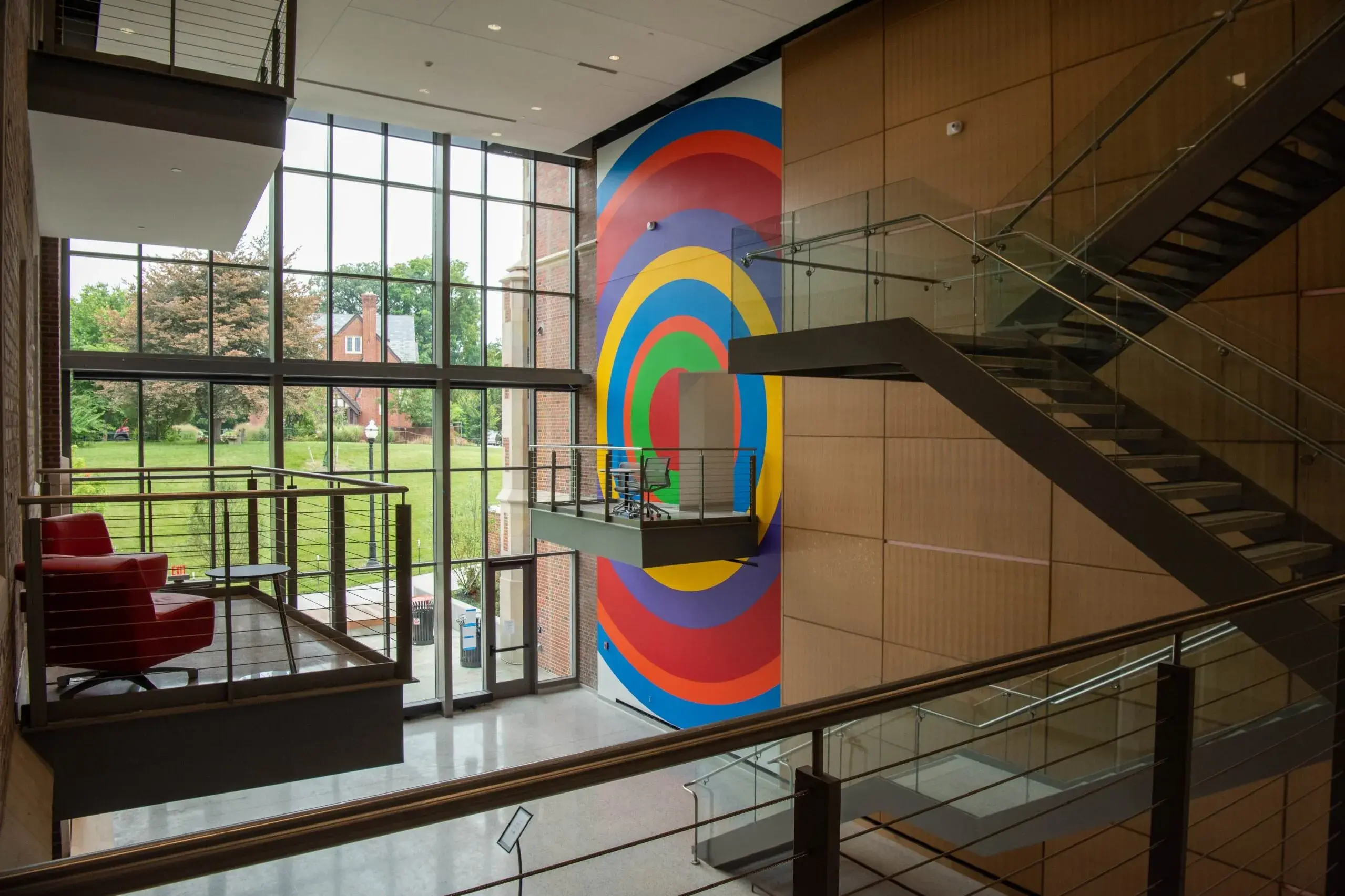 Multistory atrium space with full height wall painting in one section near the windows. The painting is made of concentric circles of vibrant colors. There is a small balcony near the middle of the painting and there are other balconies and stairs in the image.