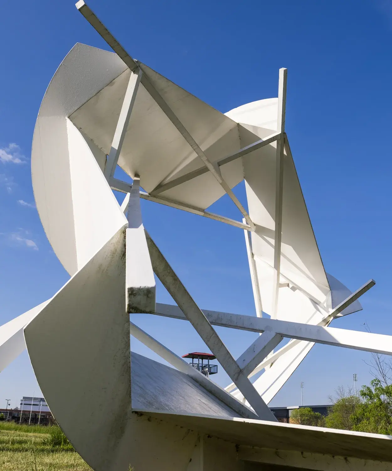 An abstract white sculpture sits on grass in front of a sunny blue sky