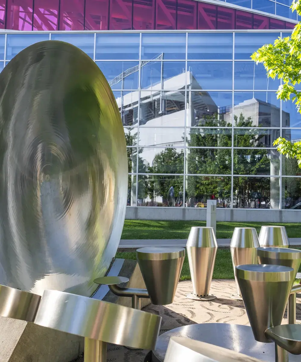 Multiple silver metal drums of various types sit on a textured area in the grass. There is a glass building in the background.