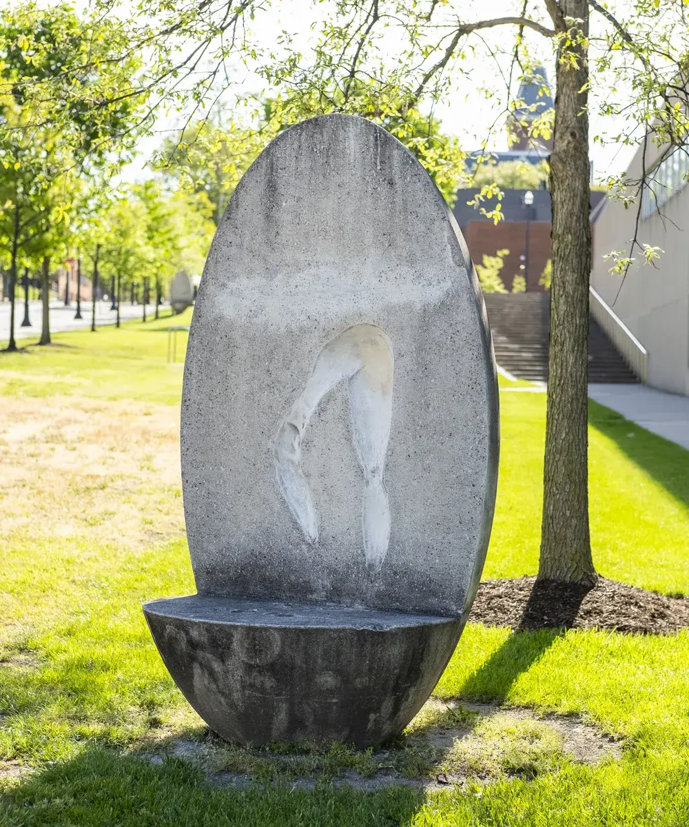 Oval concrete sculptural bench with an impression of a person's legs in a movement position on the vertical back portion