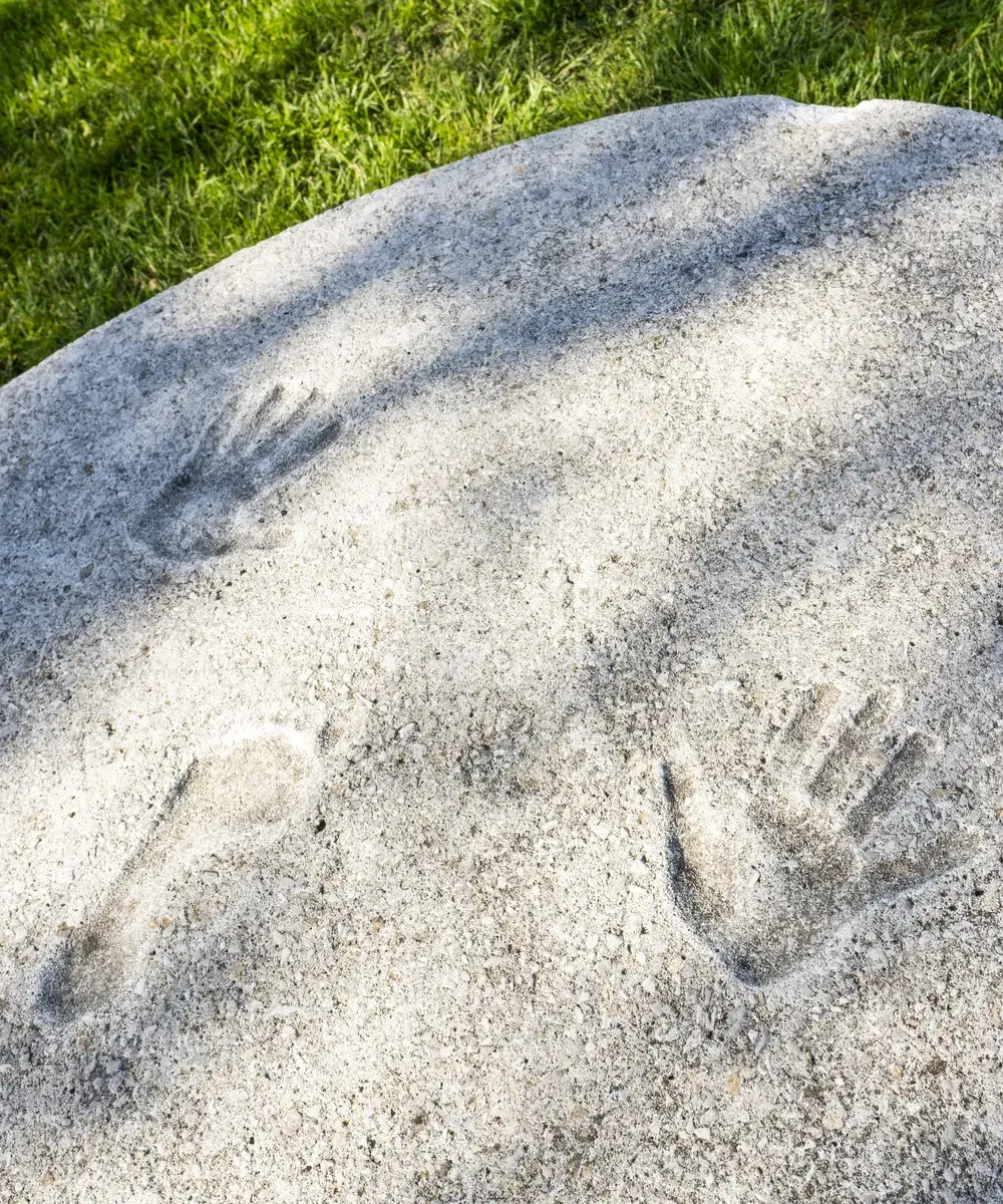 Top of an oval concrete object with an impression of a person's two hands with a foot impression between them