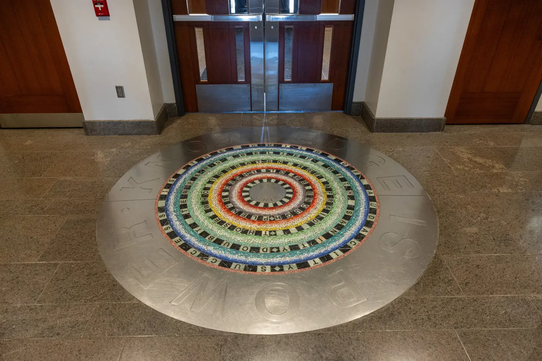 Circular floor installation with thick metal band around the edge and a black and white and multicolored mosaic pattern in the center. The words "knowledge is power" are visible around the perimeter.