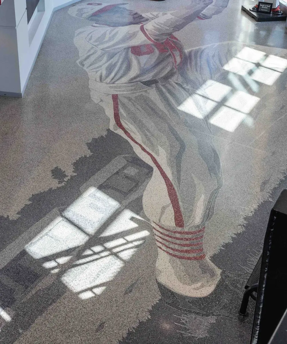 Floor design in grayscale and red shows a baseball player wearing a white and red uniform catching a ball. There is light from windows on the floor.