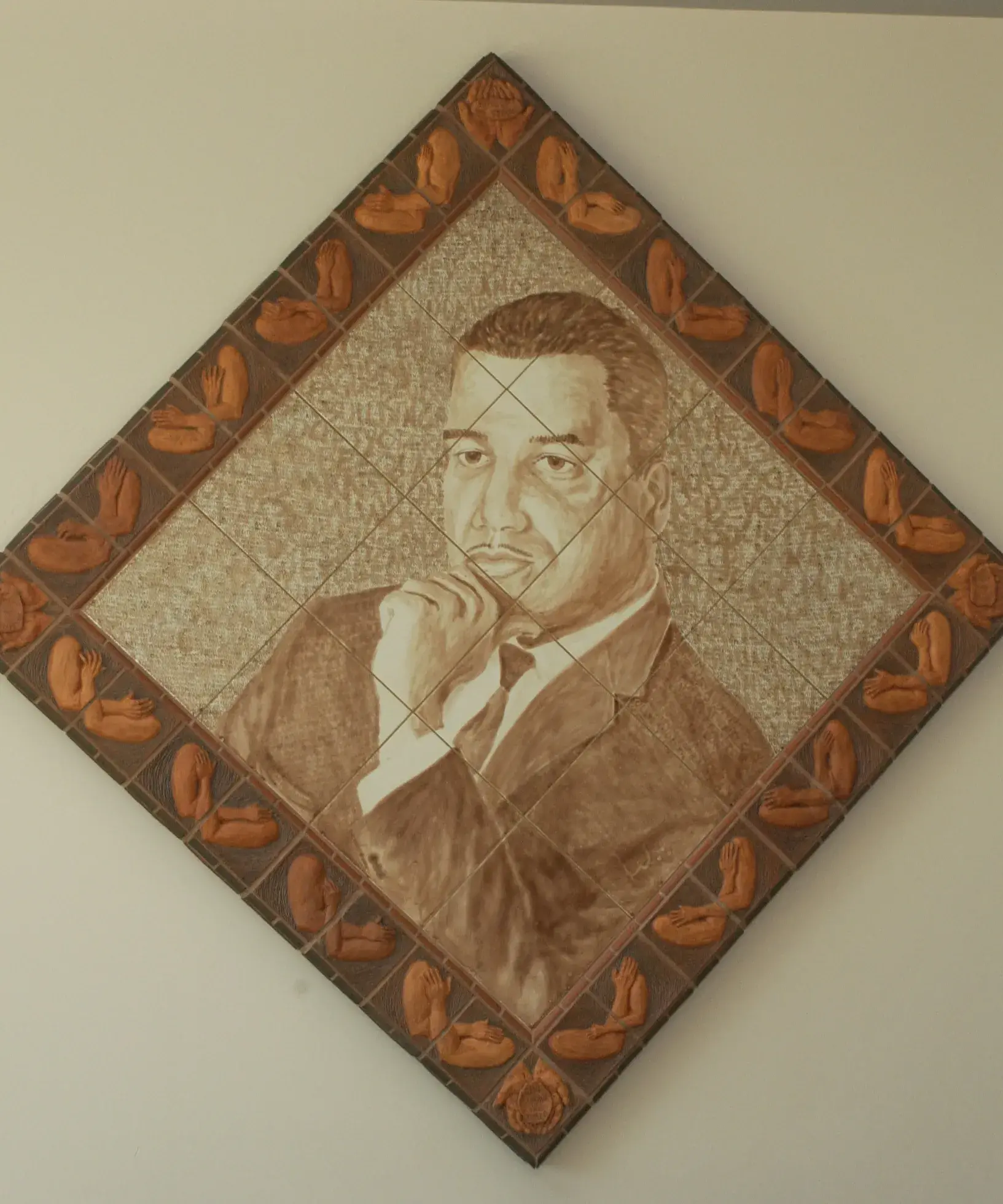 Diamond-shaped artwork made of a grid of tiles shows a historical man's head and shoulders in sepia tones. There is a border around the artwork with crossed arms in a darker brown.