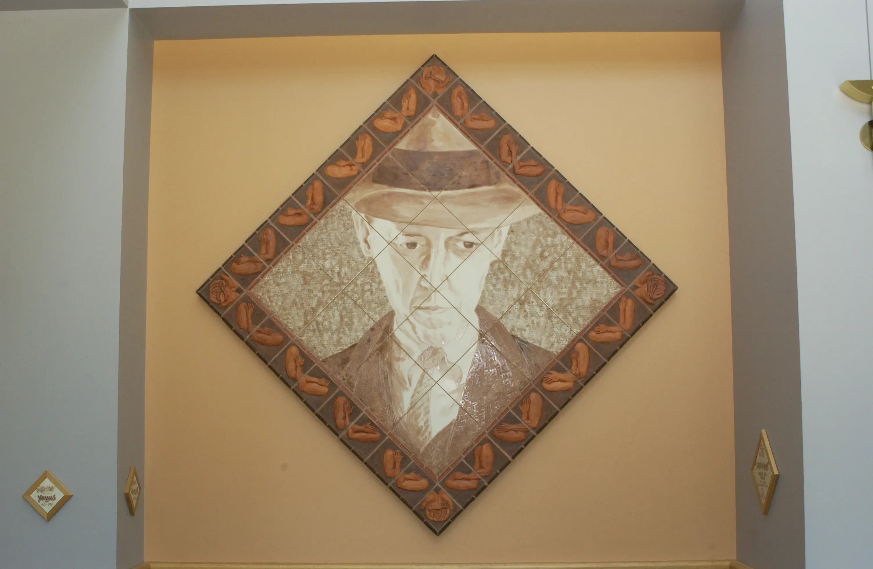 Diamond-shaped artwork made of a grid of tiles shows a historical man's head and shoulders in sepia tones. There is a border around the artwork with crossed arms in a darker brown.