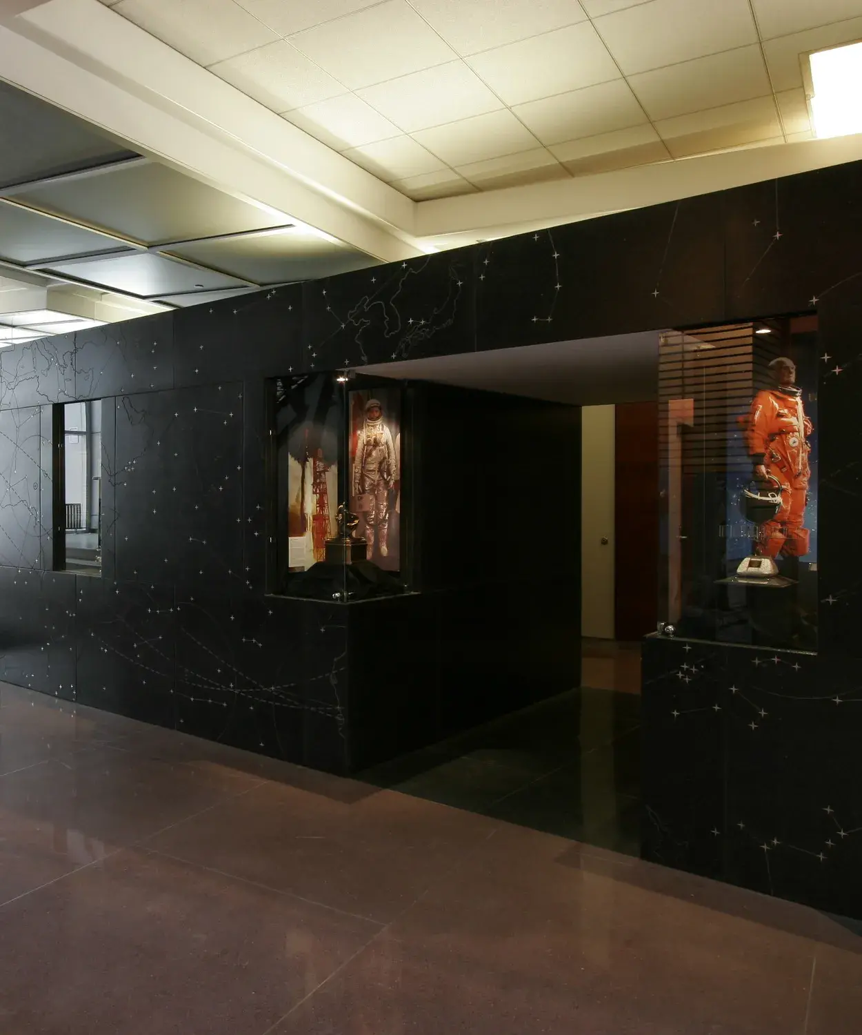 A black wall with star maps on it has inset cases with images of an astronaut and a rocket inside. 