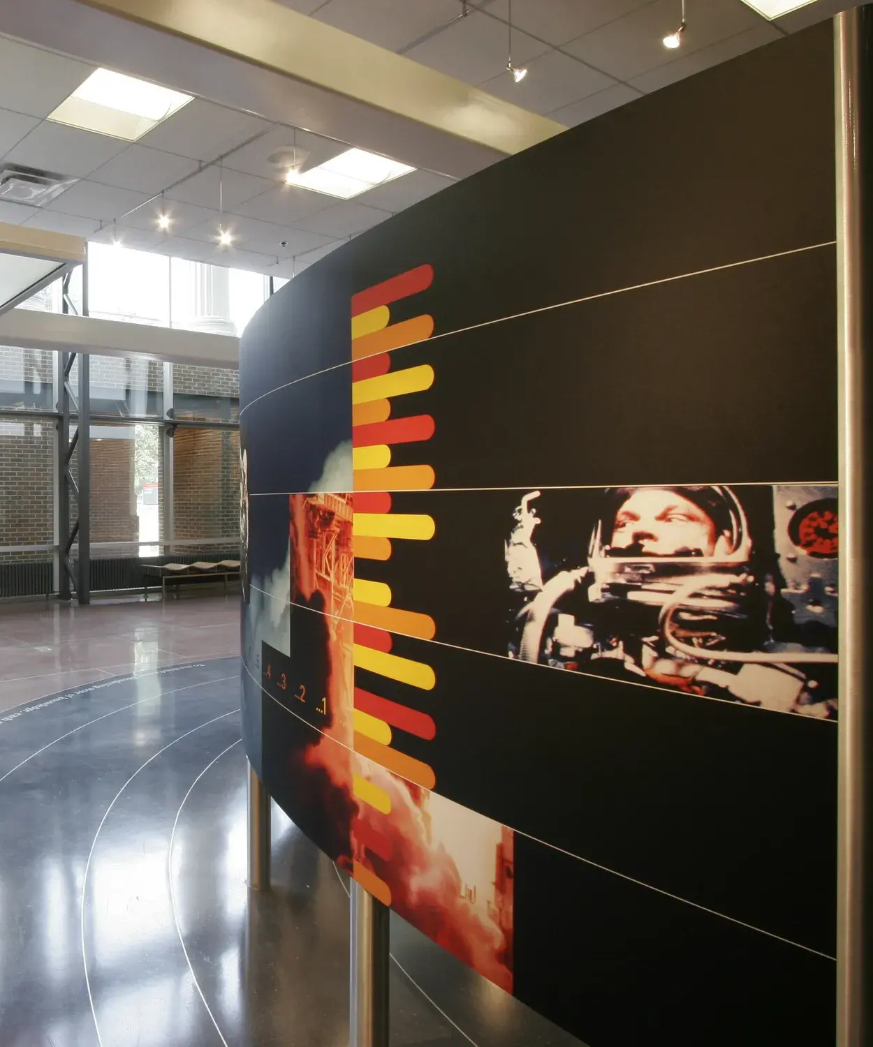 Images of an astronaut and a space shuttle on a black background and a timeline on a white background are printed on 2 curved panels held up on metal legs. The shiny floor has rings on it.