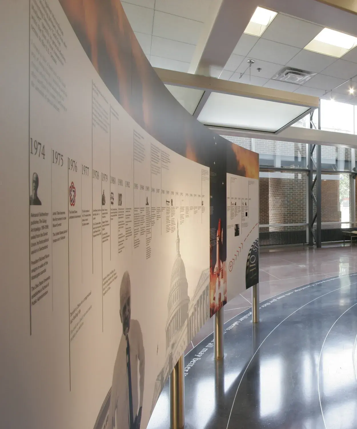 Images of an astronaut and a space shuttle on a black background and a timeline on a white background are printed on 2 curved panels held up on metal legs. The shiny floor has rings on it.