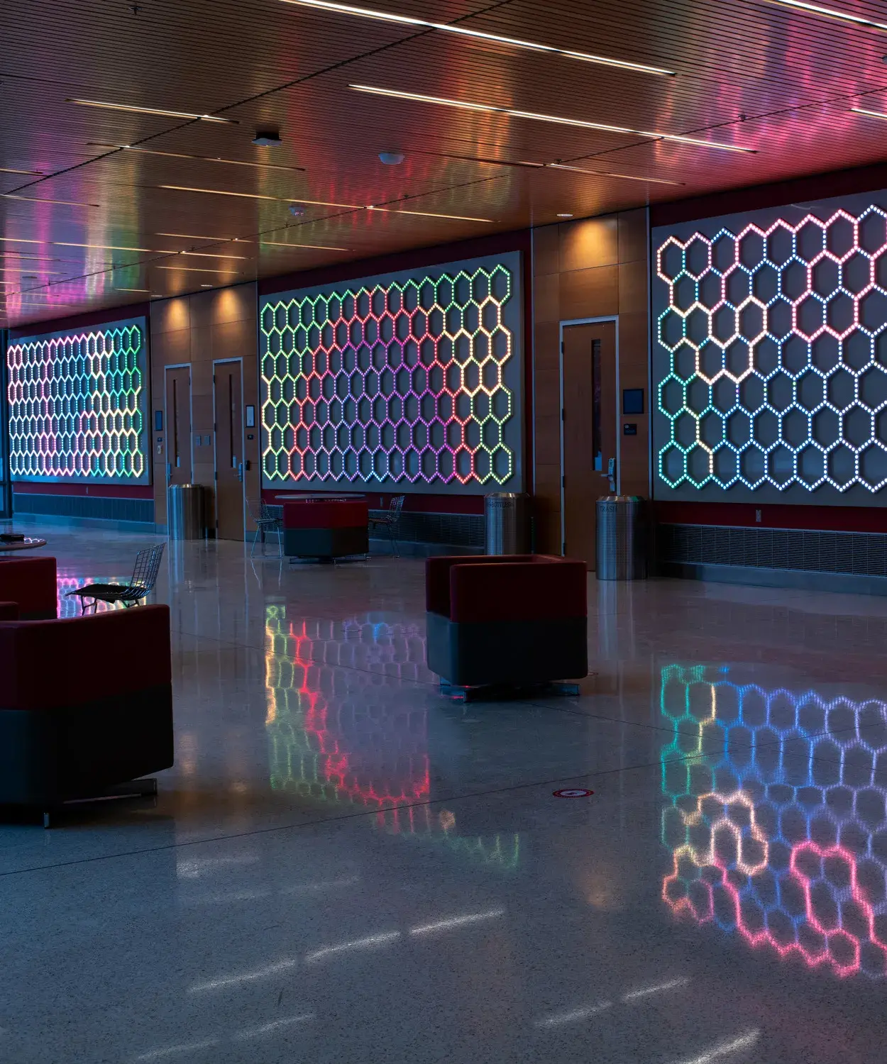 Lobby space with three walls of a light installation consisting of small bulbs in a honeycomb pattern. The lights have different patterns of colors and reflect onto the floor and ceiling.