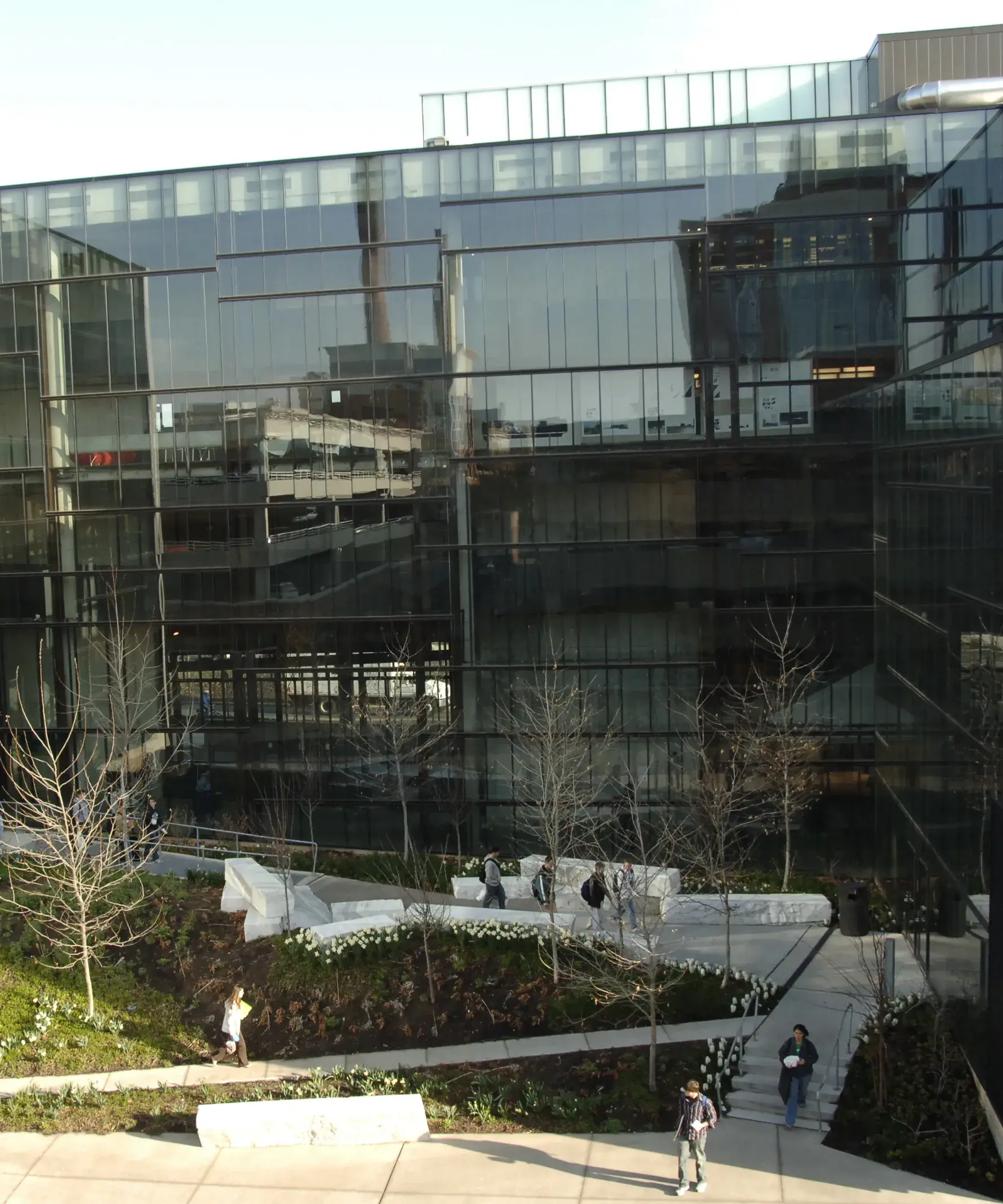 View from above of slabs of white and gray marble which sit alongside a walkway in a courtyard with trees, next to a glass building walls