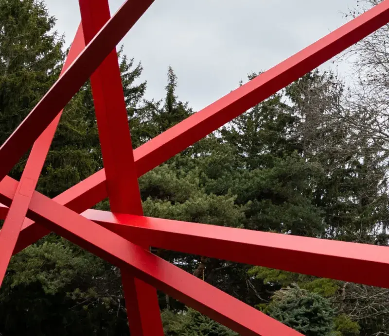 Close up of an outdoor sculpture of 5 intersecting red bars of varying lengths