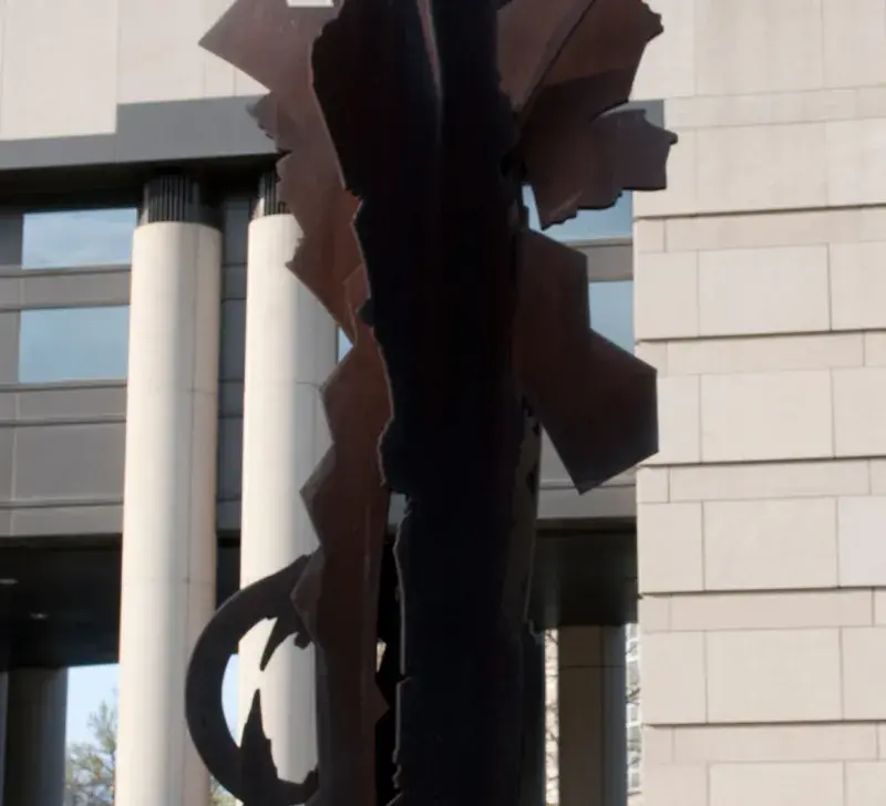 A metal sculpture centered with a white cement building in background.